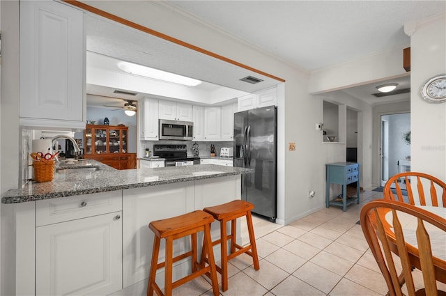 kitchen with kitchen peninsula, ceiling fan, dark stone countertops, appliances with stainless steel finishes, and white cabinetry