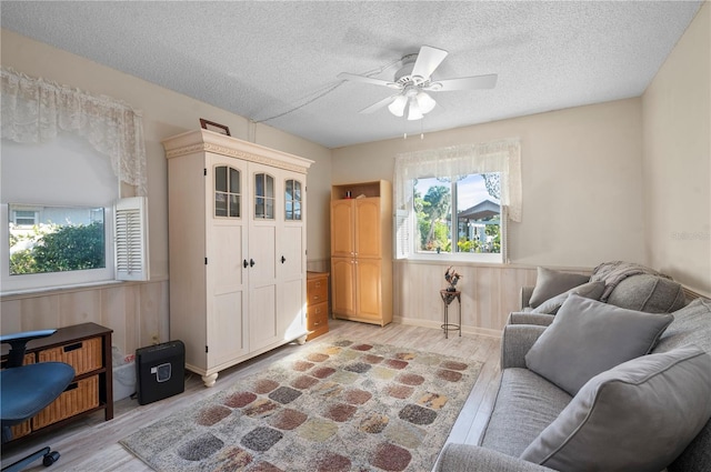 interior space with ceiling fan, a textured ceiling, wooden walls, and light hardwood / wood-style flooring