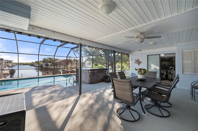 view of swimming pool featuring ceiling fan, a water view, glass enclosure, a patio area, and a hot tub