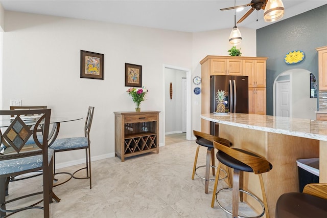 kitchen with stainless steel refrigerator, light stone countertops, ceiling fan, decorative light fixtures, and light brown cabinetry