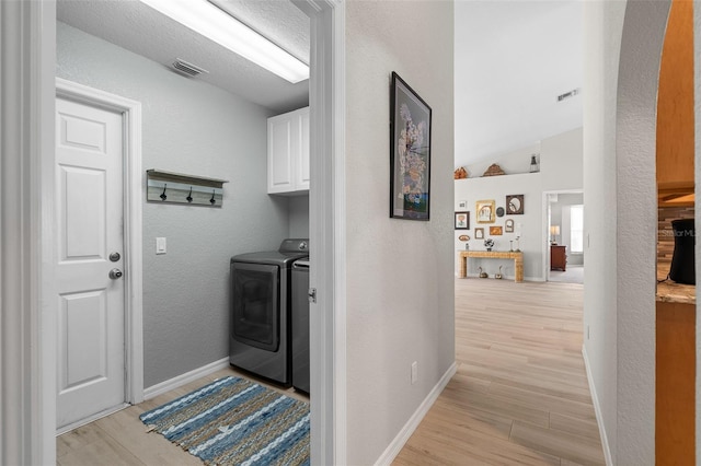 clothes washing area with washer and clothes dryer, light hardwood / wood-style floors, and cabinets