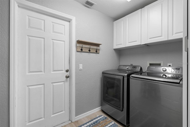 clothes washing area with cabinets, a textured ceiling, light wood-type flooring, and washer and clothes dryer