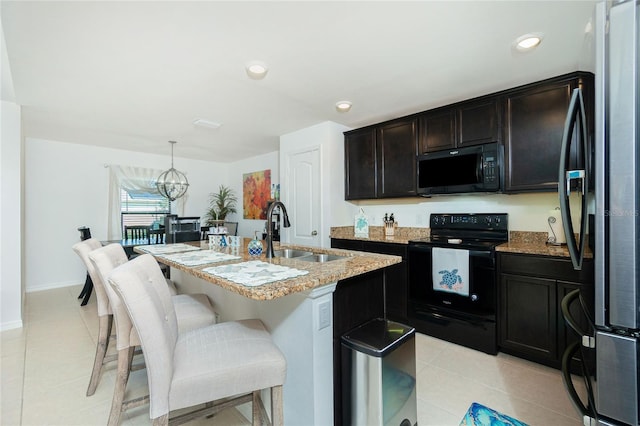 kitchen with black appliances, sink, hanging light fixtures, light stone countertops, and an island with sink