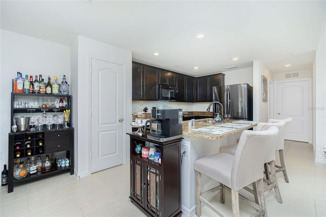 kitchen featuring sink, stainless steel fridge, a breakfast bar area, a kitchen island with sink, and light tile patterned floors