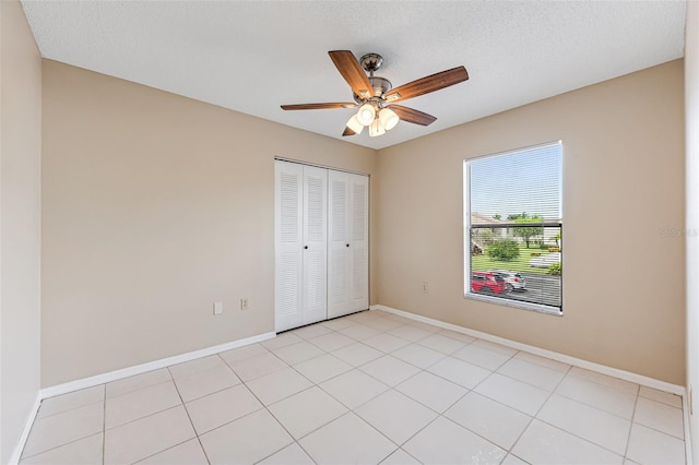 unfurnished bedroom with ceiling fan, a closet, light tile patterned floors, and a textured ceiling