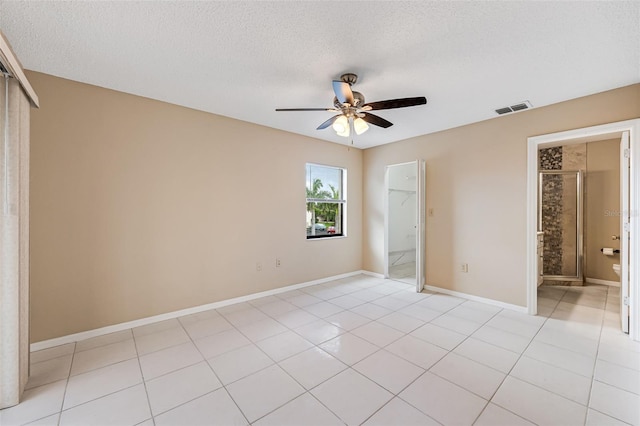 unfurnished bedroom with a textured ceiling, ensuite bath, ceiling fan, and light tile patterned flooring