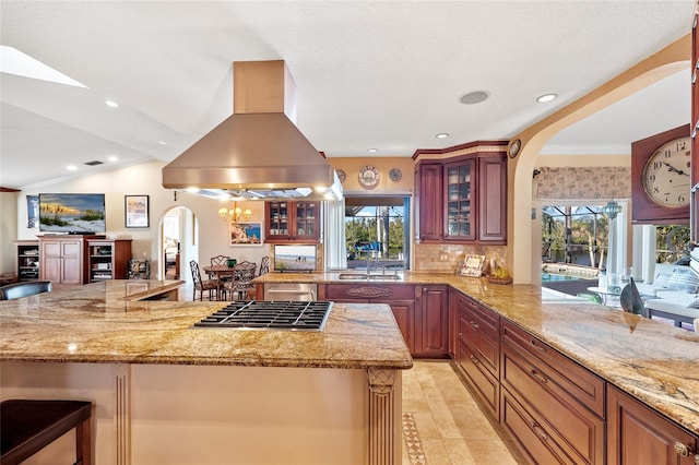 kitchen with kitchen peninsula, a kitchen bar, ornamental molding, island range hood, and stainless steel gas cooktop