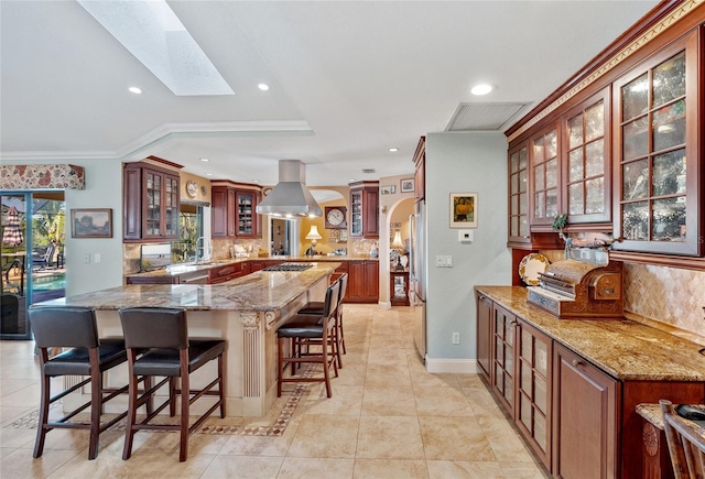 kitchen with a skylight, light stone counters, island range hood, and decorative backsplash