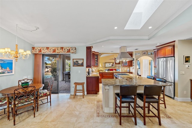 kitchen with a skylight, light stone countertops, stainless steel appliances, island exhaust hood, and ornamental molding