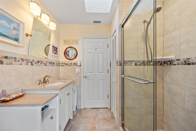 bathroom with a skylight, tile patterned flooring, an enclosed shower, vanity, and tile walls