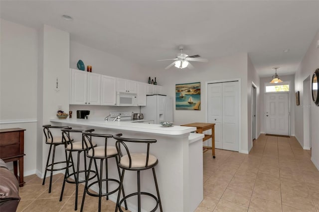 kitchen with kitchen peninsula, white appliances, decorative light fixtures, and white cabinetry