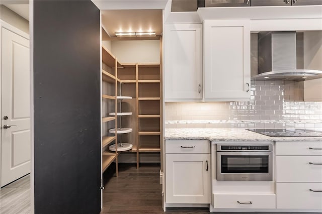 kitchen with white cabinetry, stainless steel oven, wall chimney range hood, wood-type flooring, and black electric stovetop