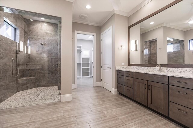 bathroom featuring a tile shower, crown molding, vanity, and ceiling fan