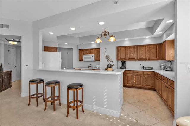 kitchen featuring white appliances, light carpet, decorative light fixtures, a notable chandelier, and kitchen peninsula