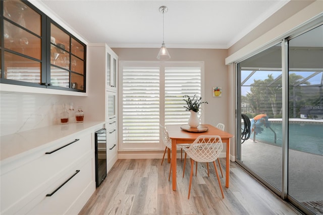 dining room with wine cooler, ornamental molding, a healthy amount of sunlight, and light wood-type flooring