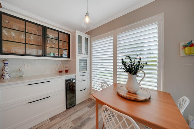 dining room with indoor bar, light wood-type flooring, beverage cooler, and ornamental molding