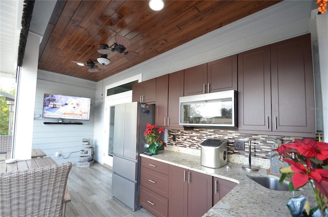 kitchen with decorative backsplash, light stone counters, stainless steel appliances, wooden walls, and light hardwood / wood-style flooring