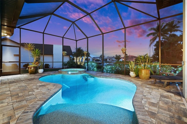 pool at dusk featuring an in ground hot tub, glass enclosure, and a patio area