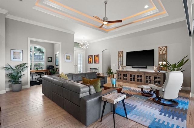 living room with ceiling fan with notable chandelier, light wood-type flooring, a raised ceiling, and ornamental molding