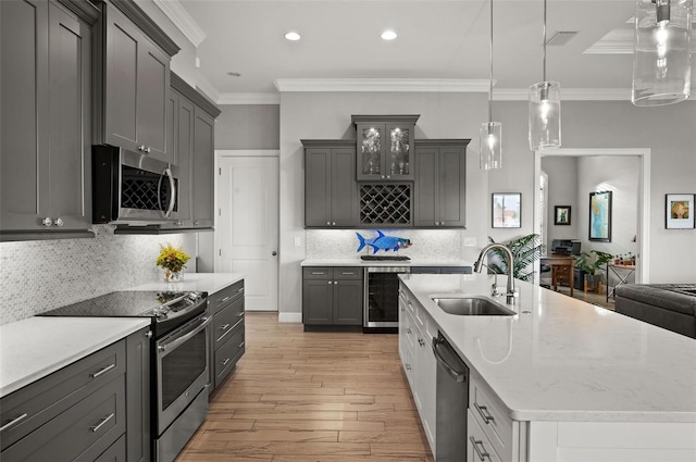 kitchen featuring sink, stainless steel appliances, light hardwood / wood-style flooring, pendant lighting, and ornamental molding