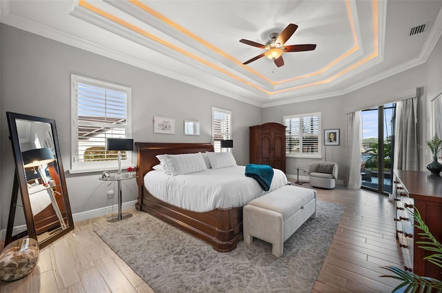 bedroom with ceiling fan, light hardwood / wood-style floors, a raised ceiling, and multiple windows