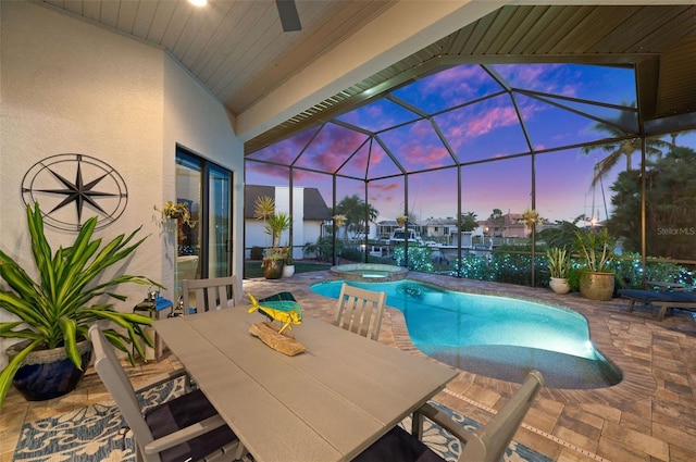 pool at dusk with glass enclosure, an in ground hot tub, and a patio