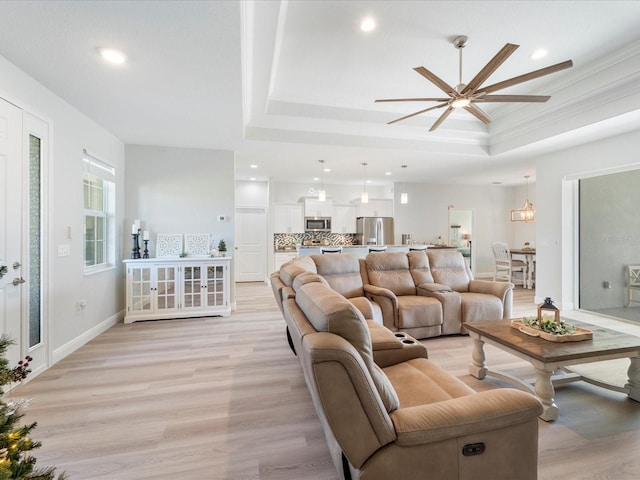 living room featuring light wood-type flooring, a raised ceiling, and ceiling fan