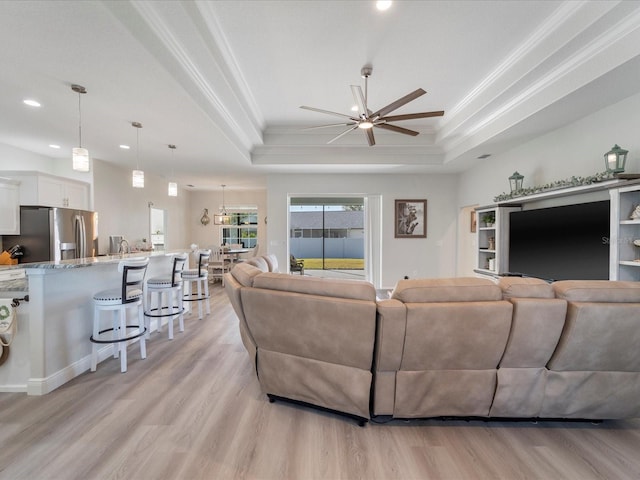 living room featuring ceiling fan, light wood-type flooring, crown molding, and a tray ceiling