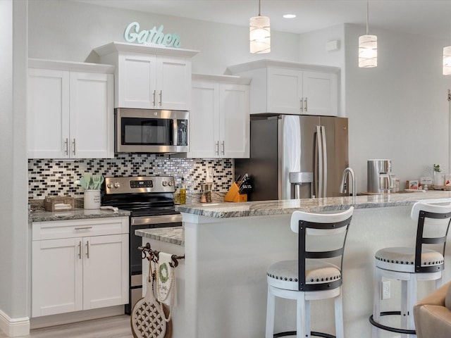 kitchen featuring white cabinetry, light stone counters, pendant lighting, a breakfast bar, and appliances with stainless steel finishes