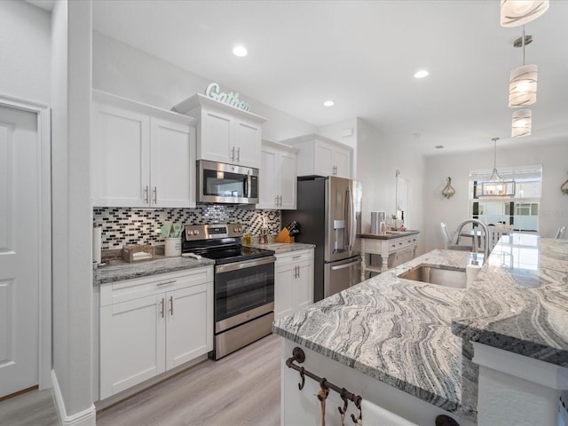 kitchen featuring sink, hanging light fixtures, light hardwood / wood-style flooring, white cabinetry, and stainless steel appliances