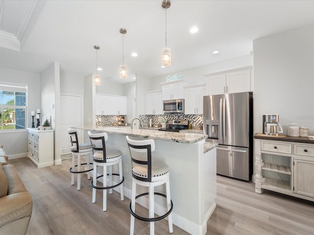 kitchen featuring white cabinets, pendant lighting, stainless steel appliances, and light hardwood / wood-style flooring