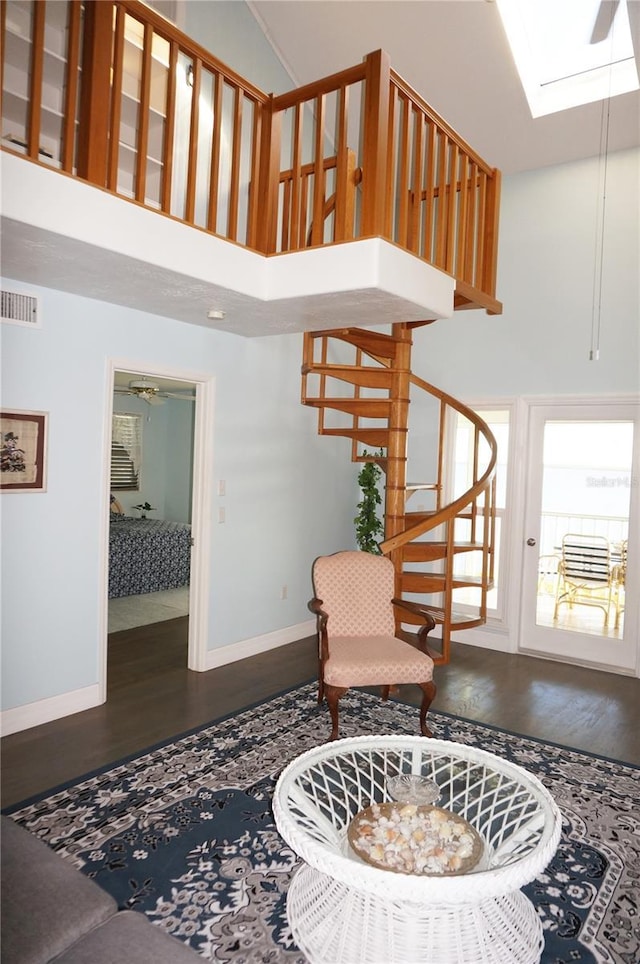 stairs with wood-type flooring, a towering ceiling, a skylight, and ceiling fan