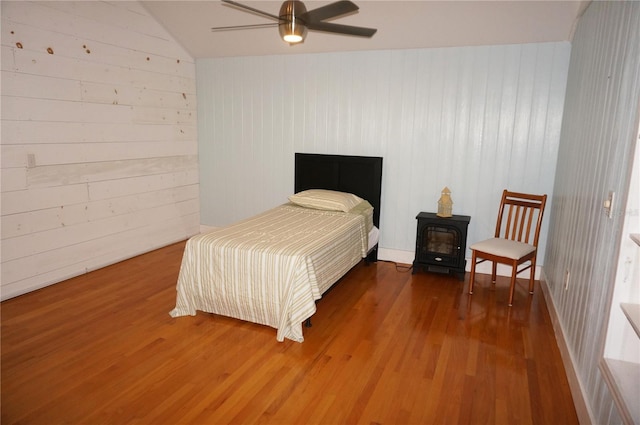 bedroom with a wood stove, ceiling fan, wood walls, lofted ceiling, and hardwood / wood-style flooring