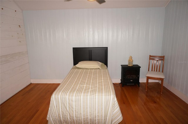 bedroom featuring hardwood / wood-style floors, ceiling fan, and wooden walls