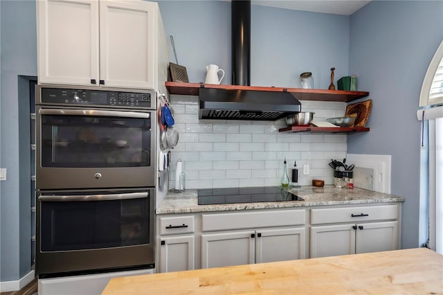 kitchen with wall chimney exhaust hood, black electric stovetop, white cabinets, and stainless steel double oven