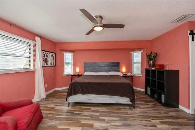 bedroom featuring a textured ceiling, dark hardwood / wood-style flooring, multiple windows, and ceiling fan