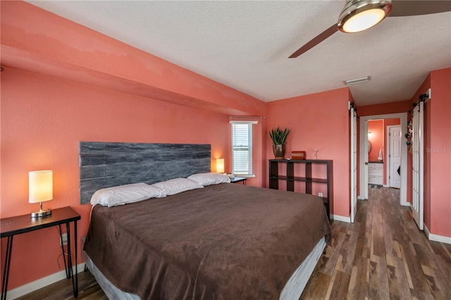 bedroom with ceiling fan, a barn door, dark hardwood / wood-style floors, a textured ceiling, and vaulted ceiling