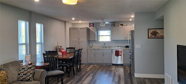 kitchen featuring light stone countertops, appliances with stainless steel finishes, ceiling fan, dark wood-type flooring, and sink