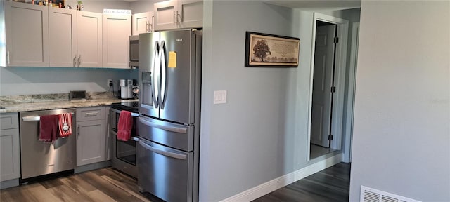 kitchen featuring gray cabinetry, light stone counters, dark hardwood / wood-style flooring, and appliances with stainless steel finishes