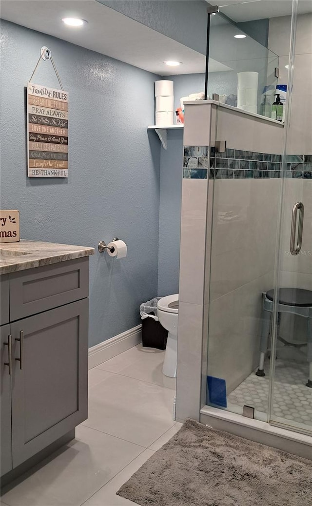 bathroom featuring tile patterned floors, vanity, a shower with shower door, and toilet