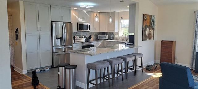 kitchen with a breakfast bar area, dark hardwood / wood-style floors, decorative light fixtures, light stone counters, and stainless steel appliances