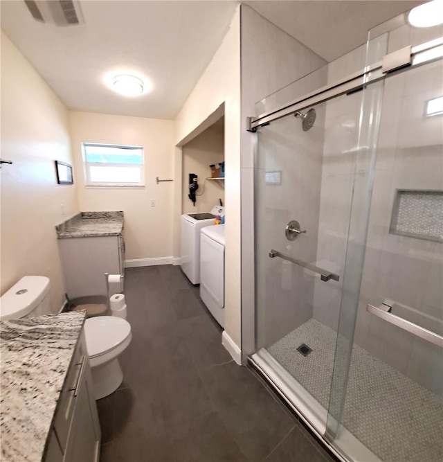 bathroom featuring vanity, tile patterned flooring, toilet, independent washer and dryer, and a shower with shower door