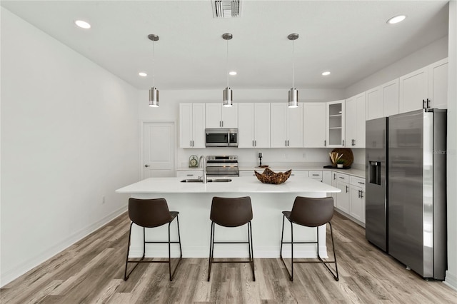 kitchen with white cabinets, appliances with stainless steel finishes, light hardwood / wood-style floors, and decorative light fixtures