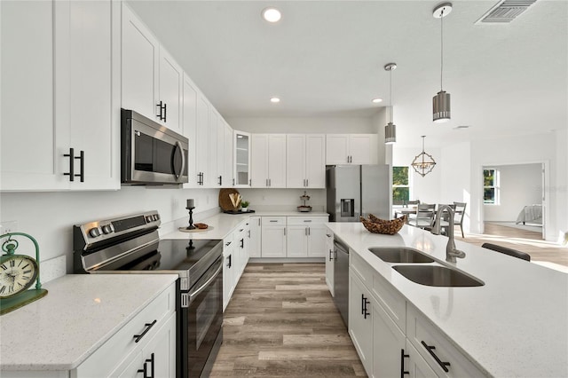 kitchen featuring sink, stainless steel appliances, light hardwood / wood-style floors, decorative light fixtures, and white cabinets