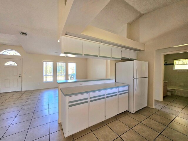 kitchen with kitchen peninsula, a textured ceiling, light tile patterned floors, white refrigerator, and white cabinetry