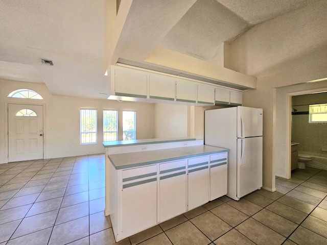 kitchen with light tile patterned flooring, white cabinetry, a textured ceiling, white fridge, and kitchen peninsula