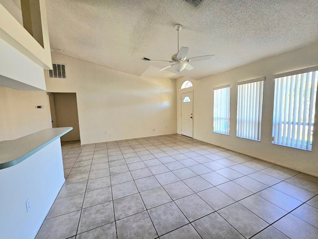 tiled empty room with ceiling fan, a textured ceiling, and vaulted ceiling