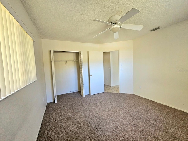 unfurnished bedroom featuring ceiling fan, a closet, light colored carpet, and a textured ceiling