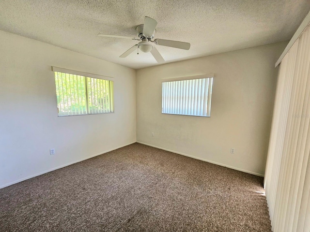 spare room with a textured ceiling, dark carpet, and a wealth of natural light