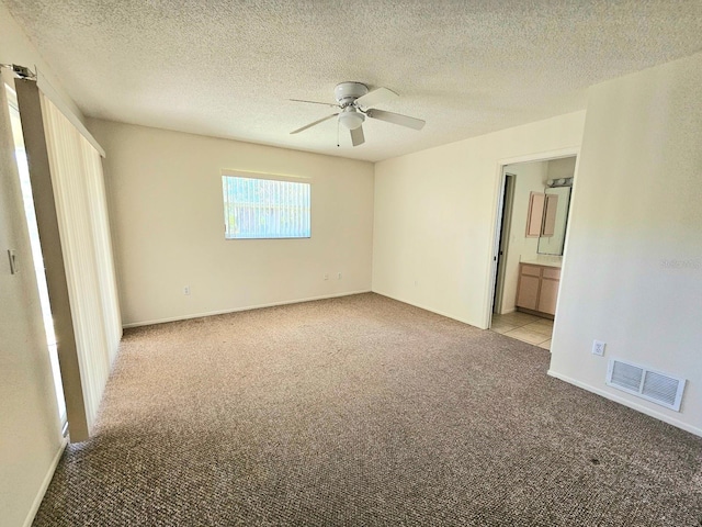 unfurnished bedroom with light carpet, a textured ceiling, ensuite bathroom, and ceiling fan